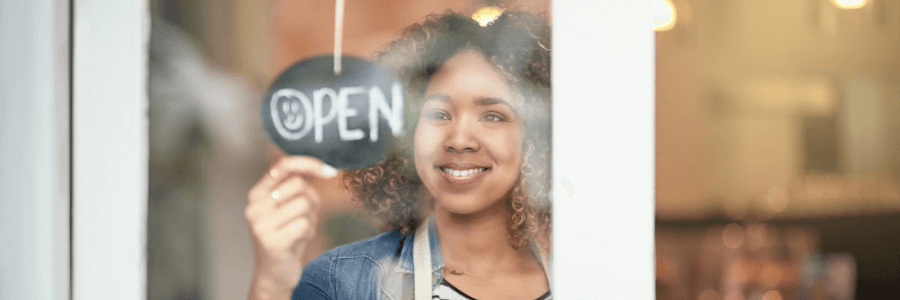 Retail employee holding "now open" sign on business door