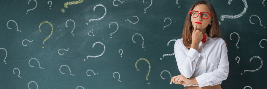 Business professional pondering something and standing in front of a chalkboard with many questions marks written on it